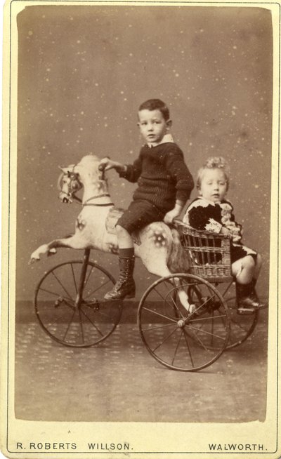 Young boy on rocking horse with young girl in wicker carriage behind, 1880s by R. Roberts Willson